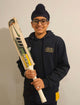 Custom made cricket bats holder smiling with bat in hand, wearing a navy hoodie, showcasing Melbourne craftsmanship.